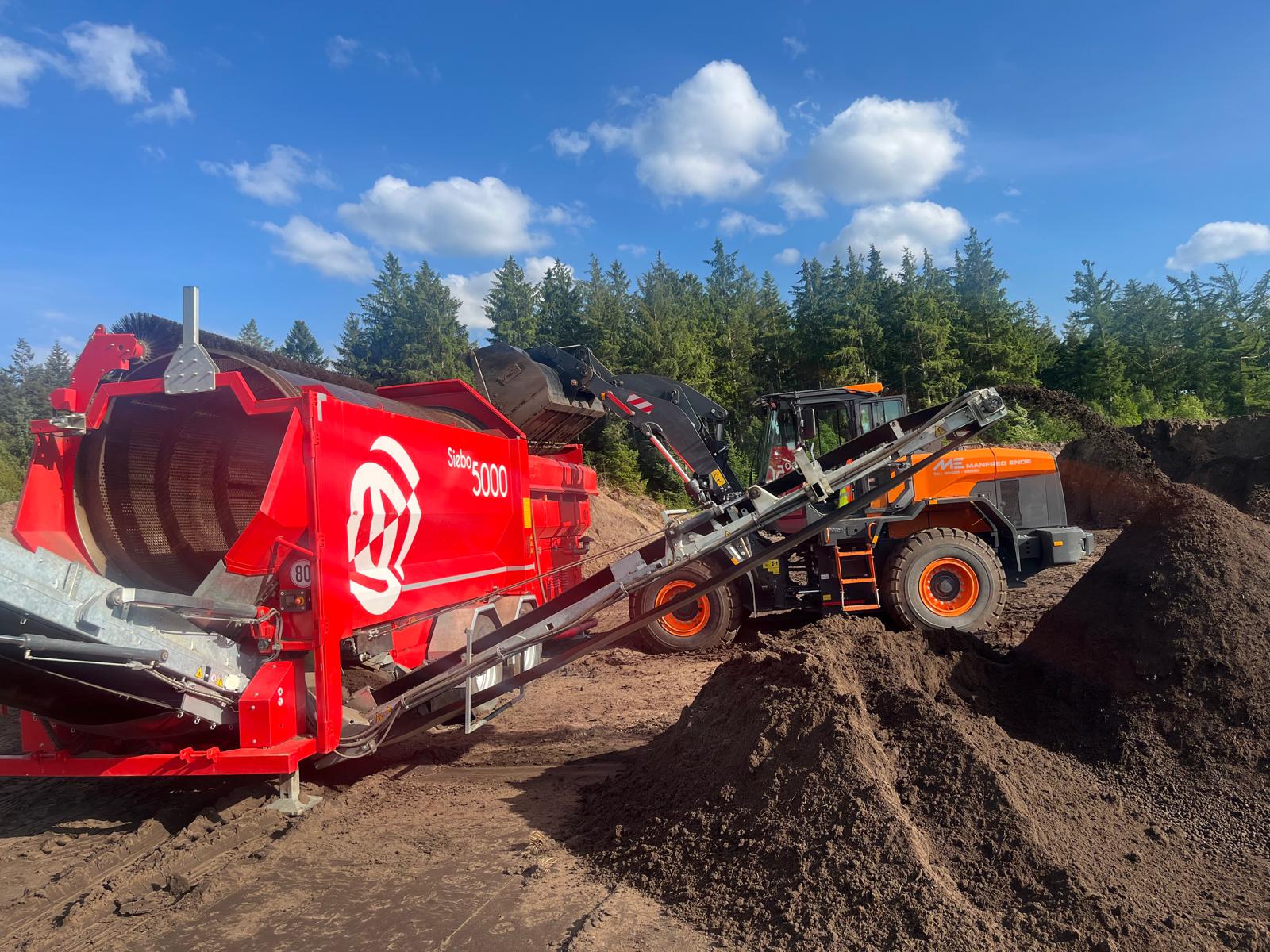 Mobile Trommelsiebmaschine Siebo 5000 mit Radlader bei der Aufbereitung von Mutterboden auf einer Baustelle. Trommelsiebmaschine zur Vermietung
